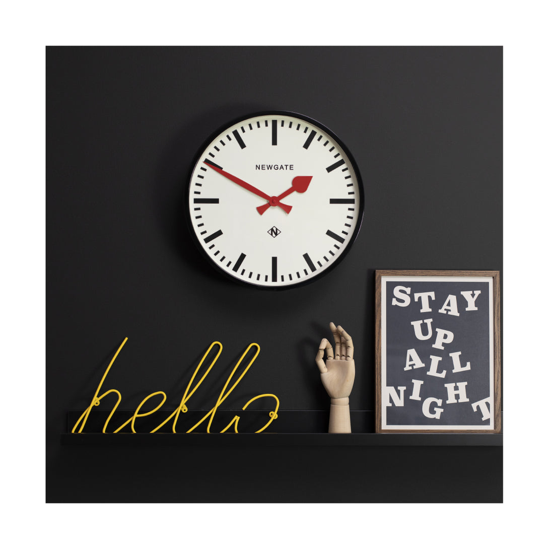 Large black station Putney wall clock by Newgate Clocks with red hands and a chunky marker dial on a black wall