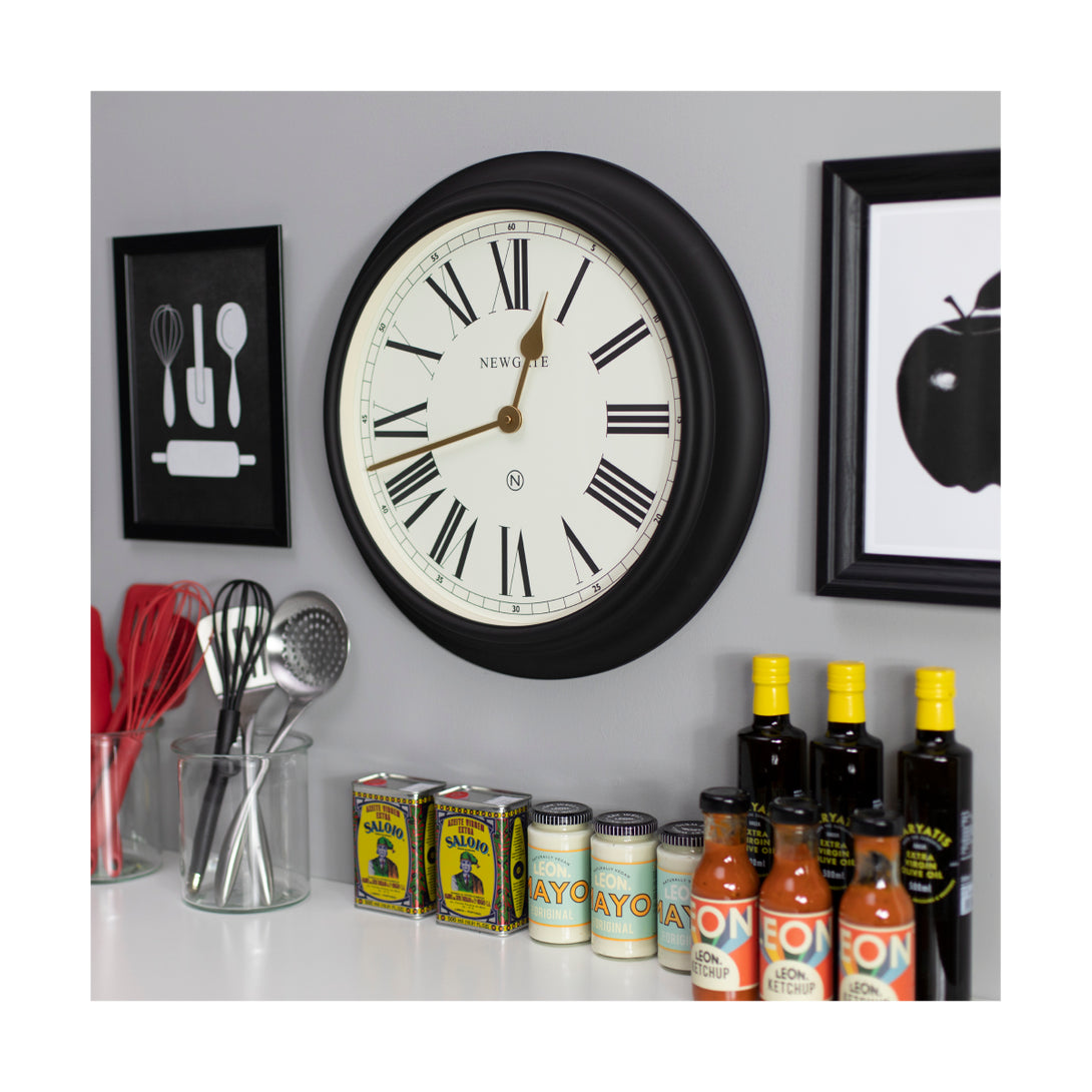 Newgate World large Chocolate Shop wall clock in Black with Gold hands and a cream Roman numeral dial in a kitchen setting