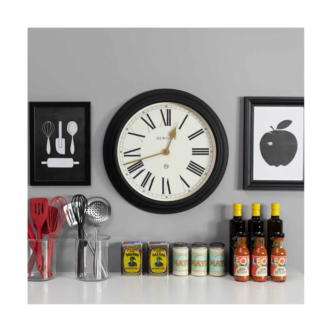 Newgate World large Chocolate Shop wall clock in Black with Gold hands and a cream Roman numeral dial in a kitchen setting