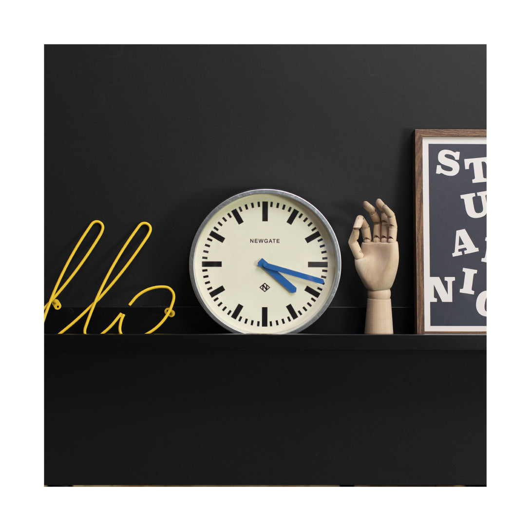 Modern industrial Luggage wall clock by Newgate Clocks with a galvanised finish, chunky marker dial and blue hands on a shelf - LUGG667GALBL