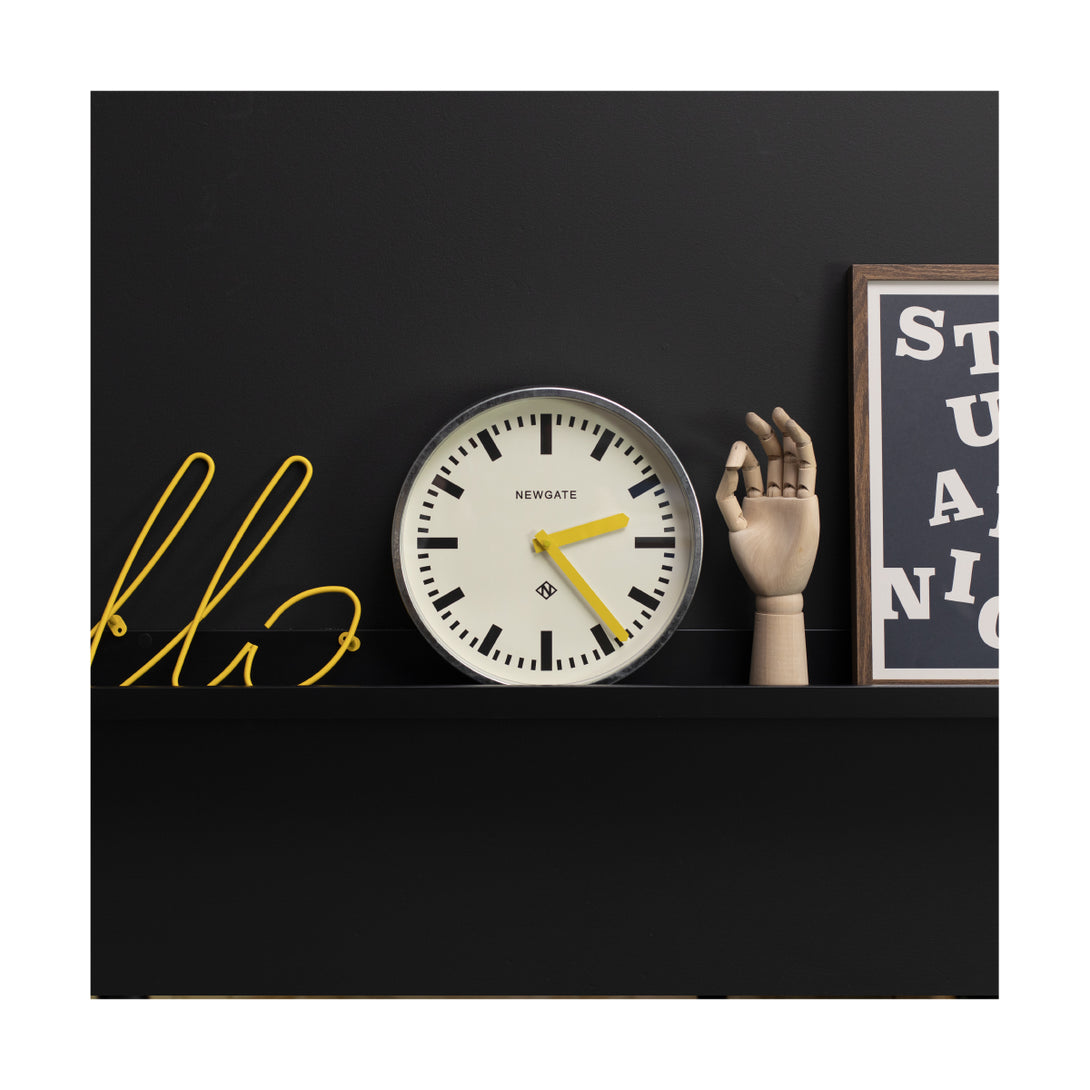 Modern industrial Luggage wall clock by Newgate Clocks with a galvanised finish, chunky marker dial and yellow hands on a shelf - LUGG667GALCY