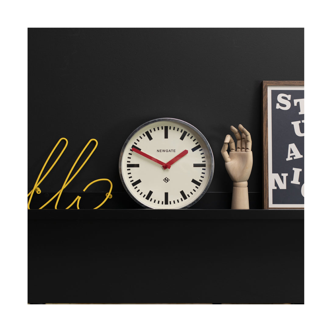 Modern industrial Luggage wall clock by Newgate Clocks with a galvanised finish, chunky marker dial and red hands on a shelf - LUGG667GALR