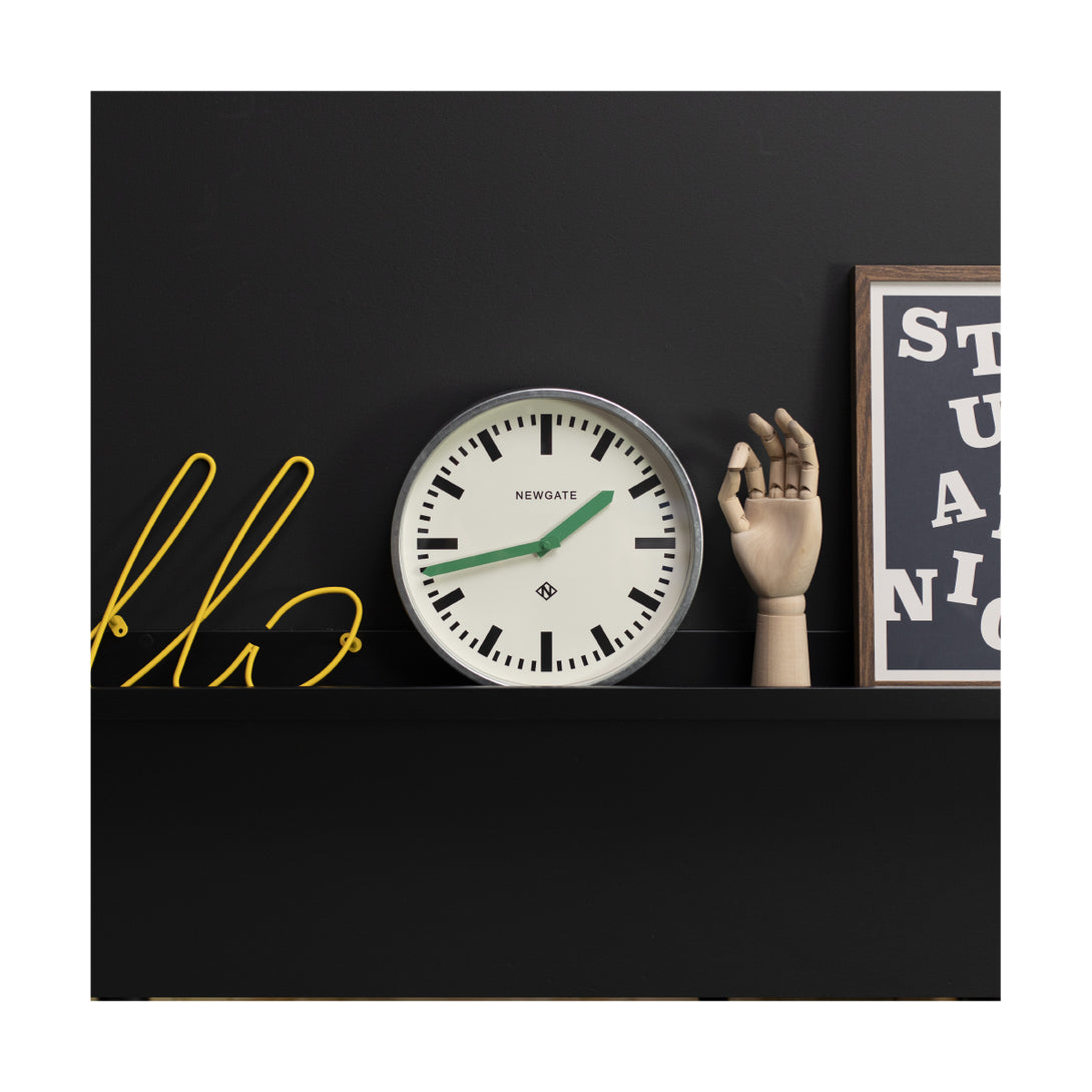 Modern industrial Luggage wall clock by Newgate Clocks with a galvanised finish, chunky marker dial and green hands on a shelf - LUGG667GALVG