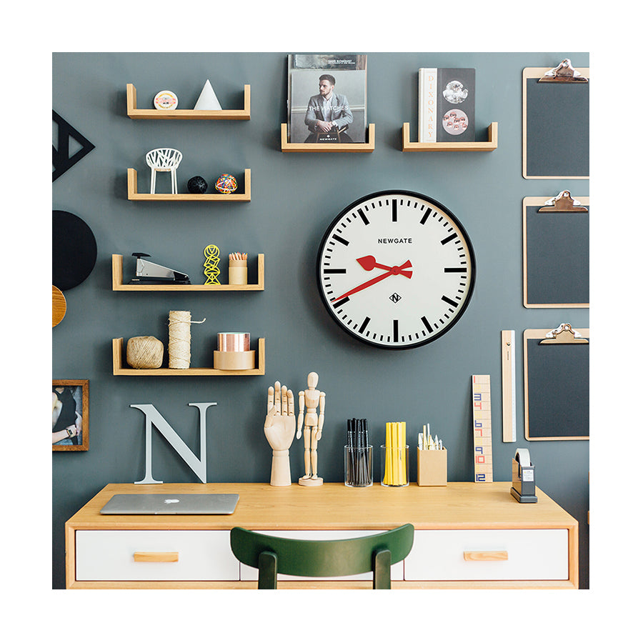 Large black station Putney wall clock by Newgate Clocks with red hands and a chunky marker dial on an office wall